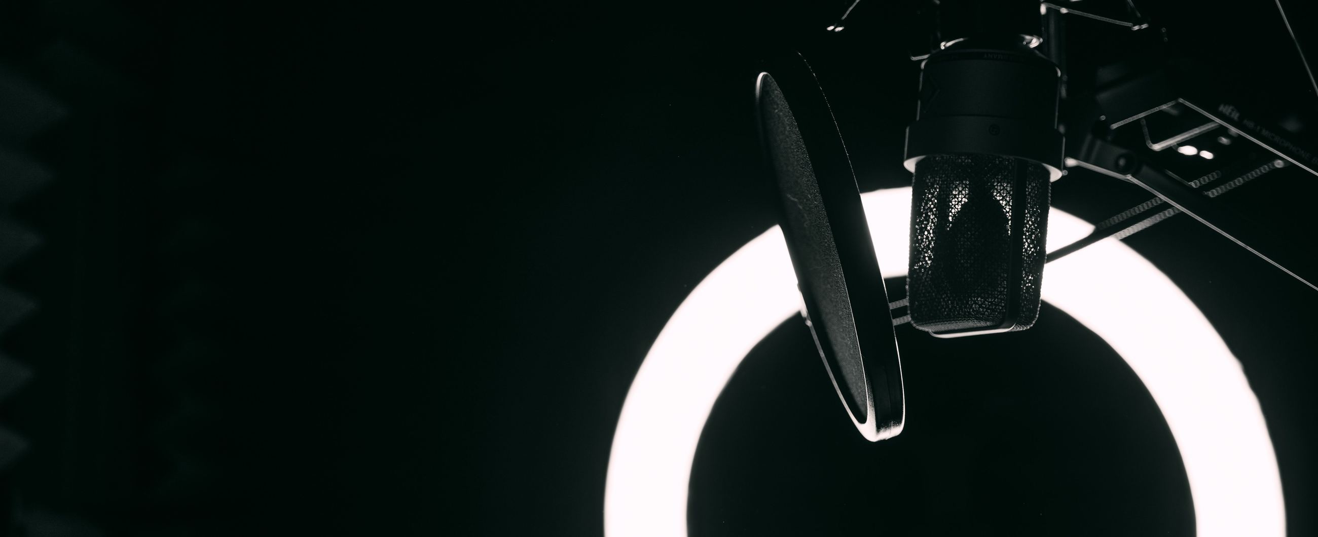 A microphone and pop shield lit by a ring light in a dark studio