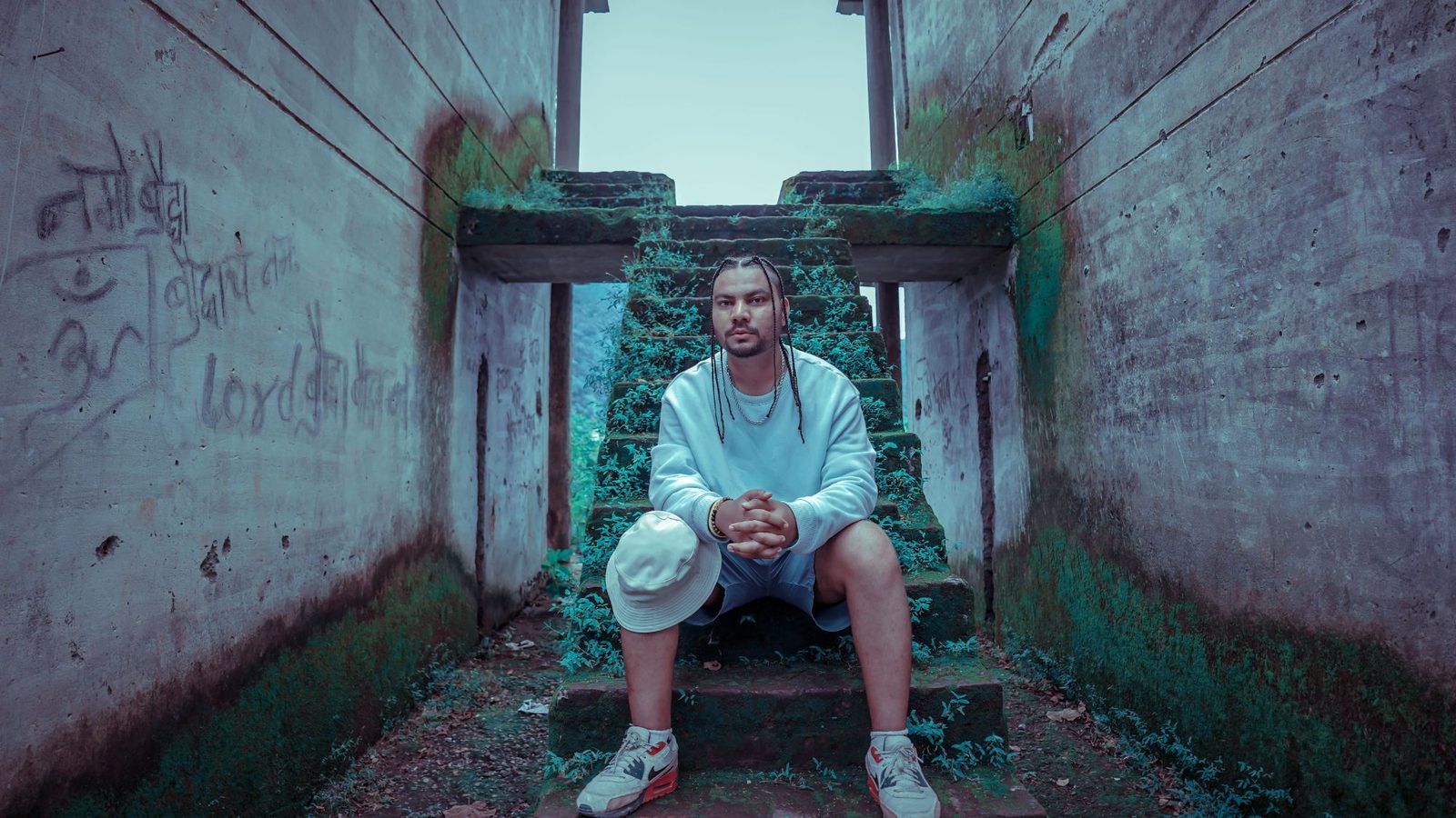 A man in a white sweatshirt sits on moss-covered concrete stairs between two graffitied walls
